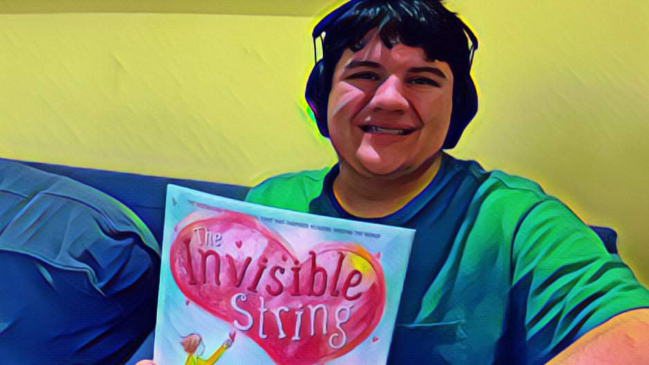 Mikey smiling, wearing headphones, holding his copy of The Invisible String.