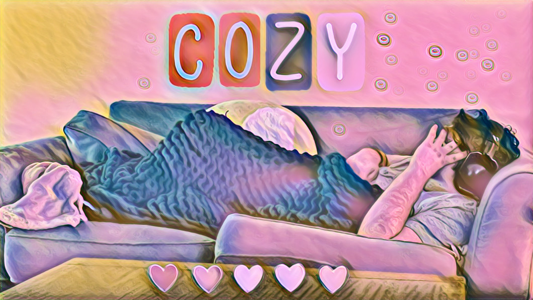 Title COZY. Mikey laying on a couch with a chunky knit weighted blanket covering him, wearing headphones.