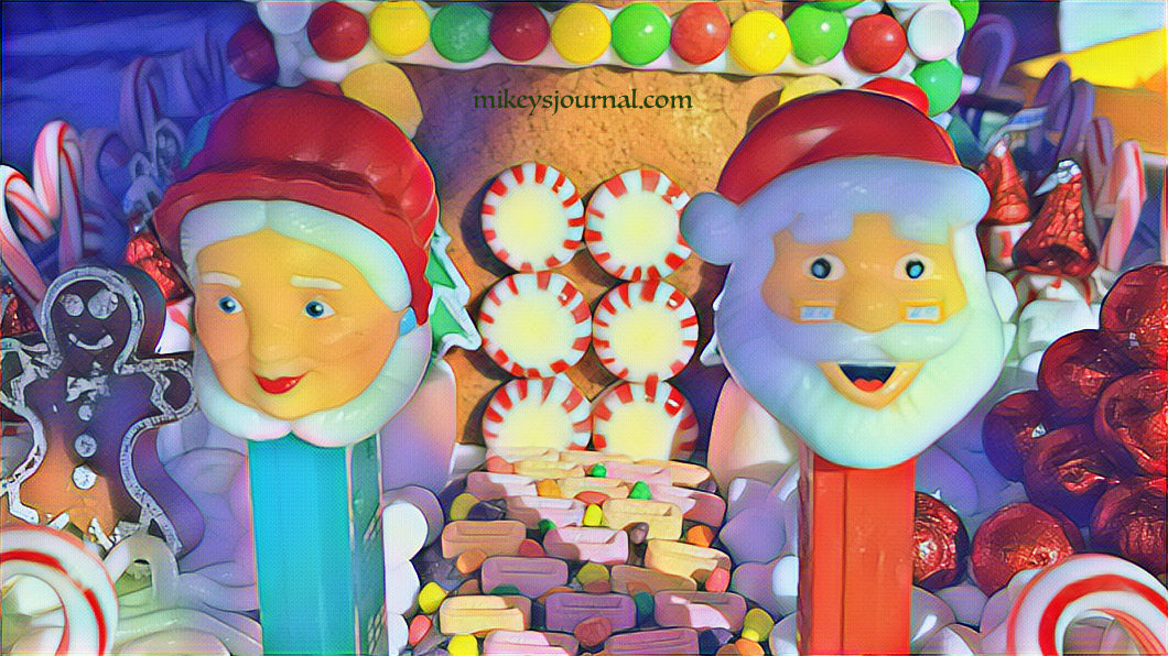 A candy-covered gingerbread house guarded by Mr. and Mrs. Claus pez dispensers.