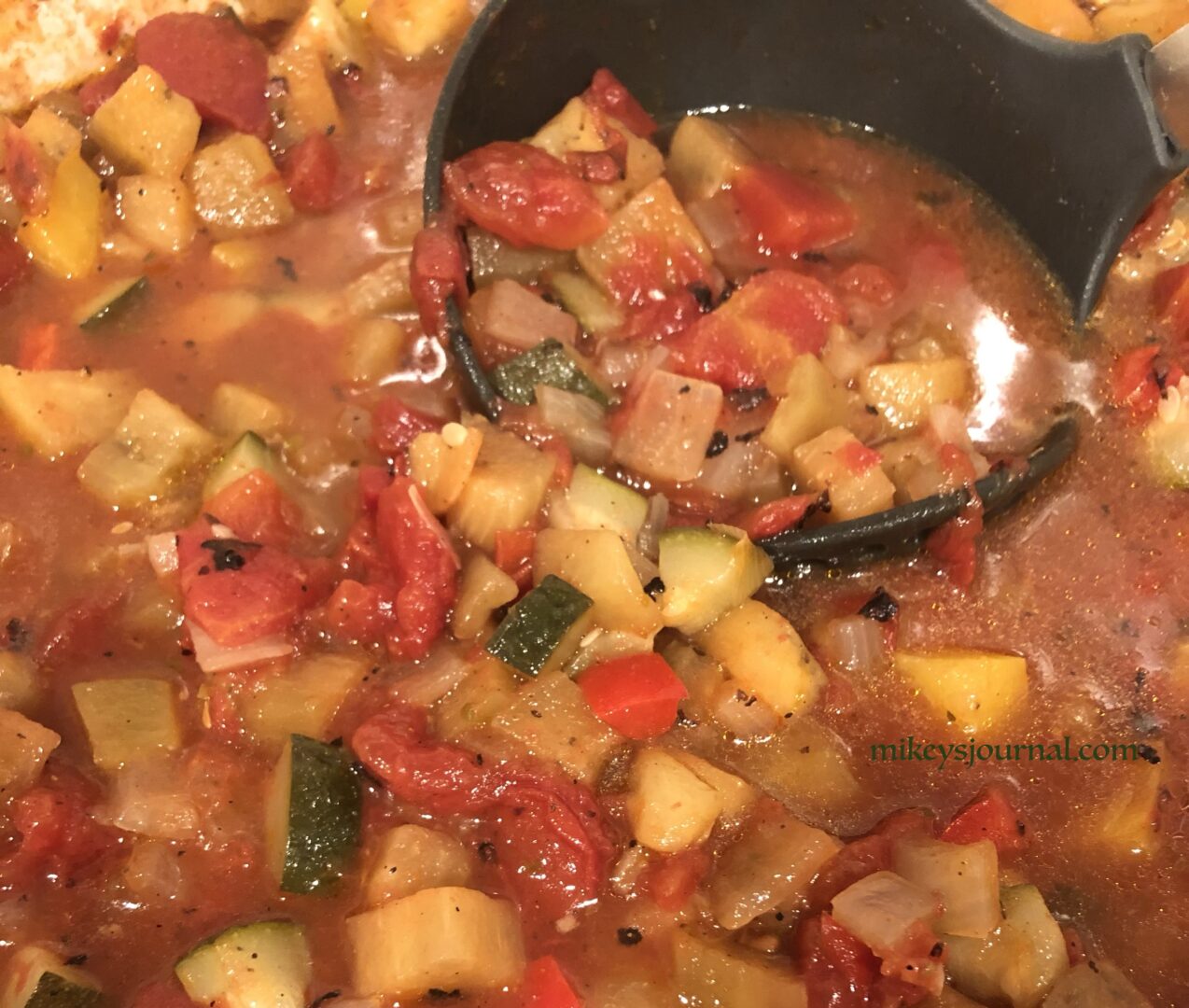 soup in a pot with visible chunks of tomato, eggplant, zucchini and yellow squash, ladle right in the pot.