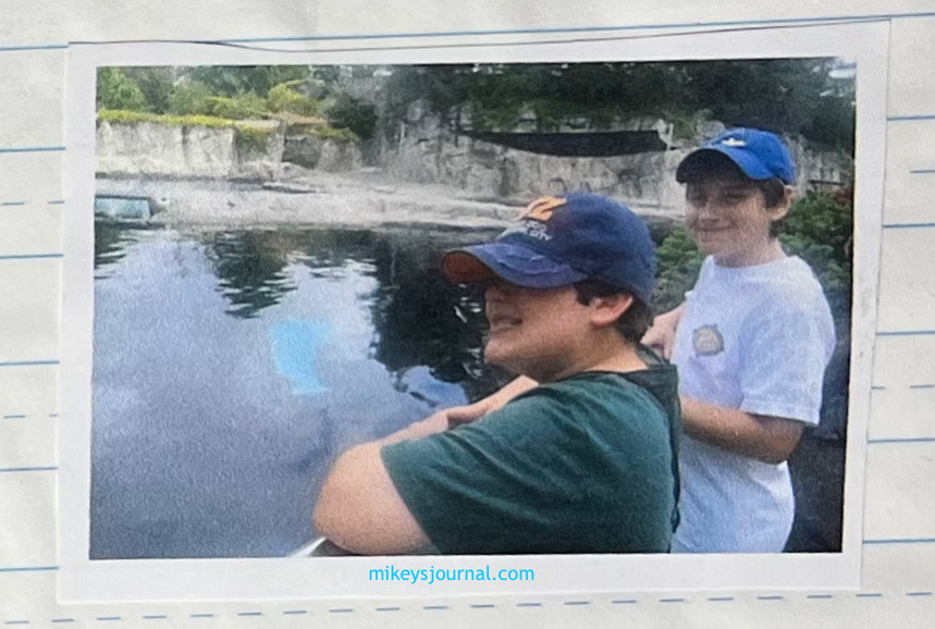 Will and Mikey standing, smiling, at the railing of an open air pool exhibit, no animal in sight.