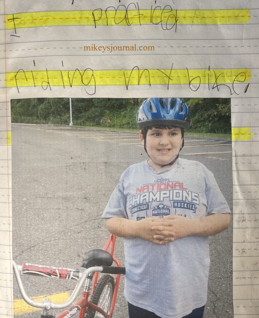 journal entry, "I practiced riding my bike." photo of Mikey smiling, hands crossed on his belly posing next to his bike.