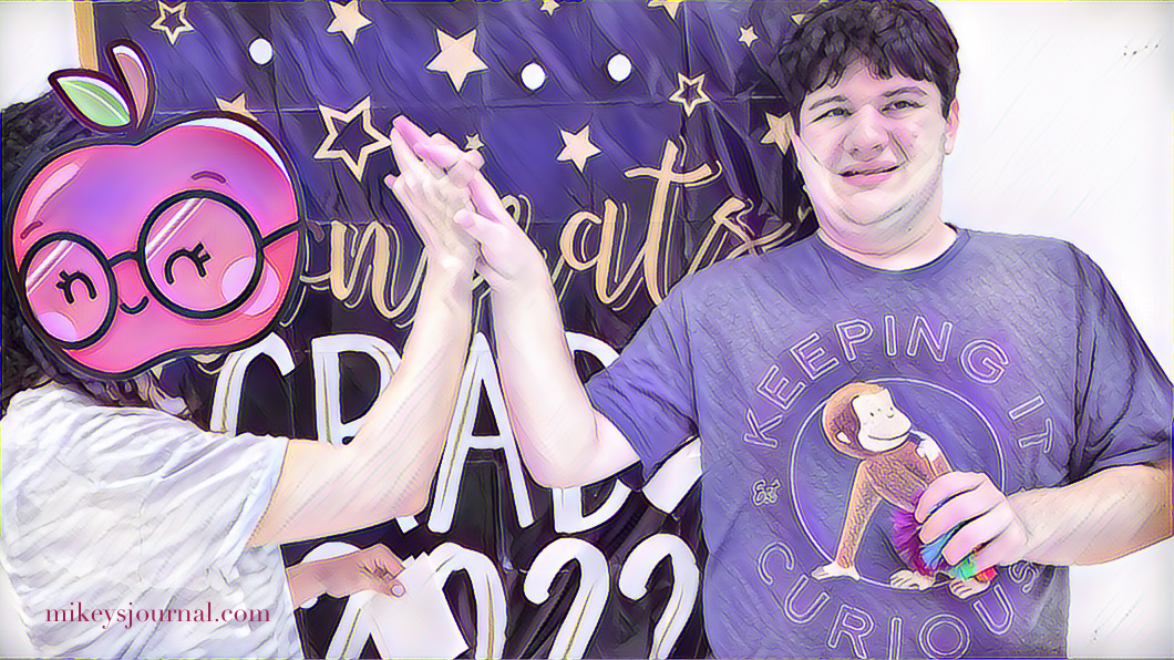 Mikey in front of a congrats banner getting a high five from his teahcer (face obscured by an apple with glasses)