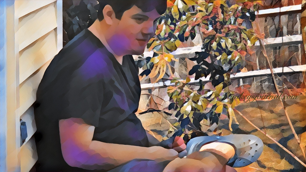 Mikey sitting against the wall on our porch, legs folded and hands in his lap with a calm look on his face