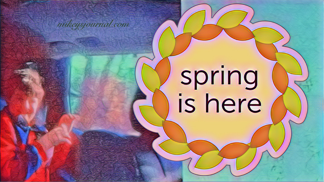 Mikey smiling wide in the back seat of the car with the window down, a large wreath sticker with the message: Spring is Here