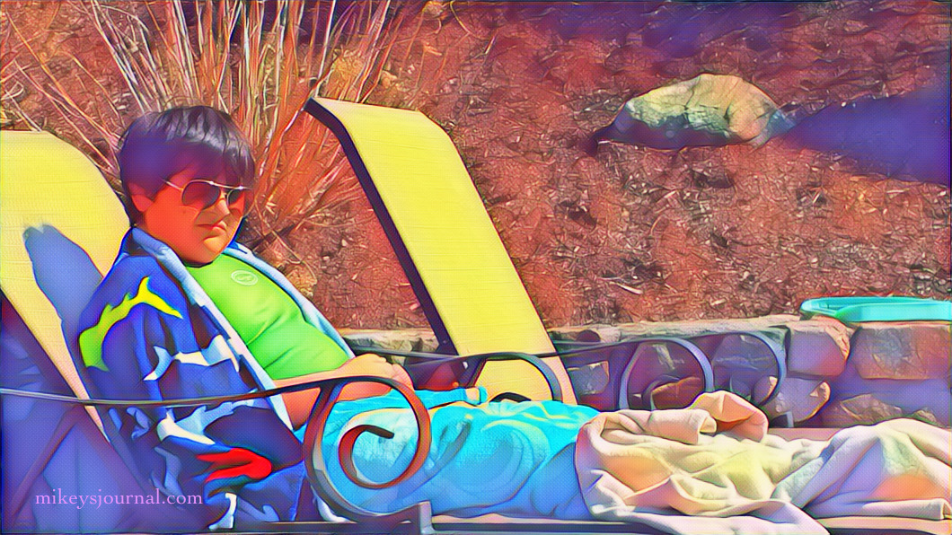 stylized photo of Mikey sitting in a lounge chair next to the pool, covered in towels with sunglasses on and a serious face