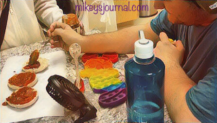 stylized photo of Mikey putting sauce on english muffins with his toys, fan and water bottle on the countertop
