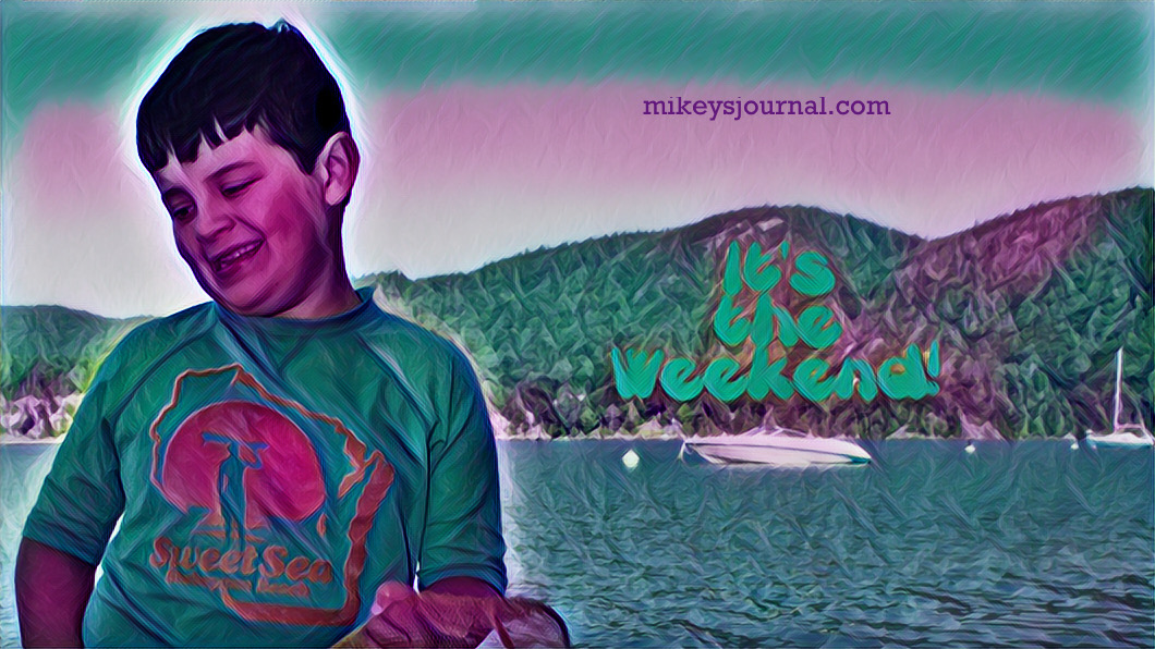 Michael smiling, standing in shallow wter on lake champlain with a speedboat and sailboat in the background and mountains